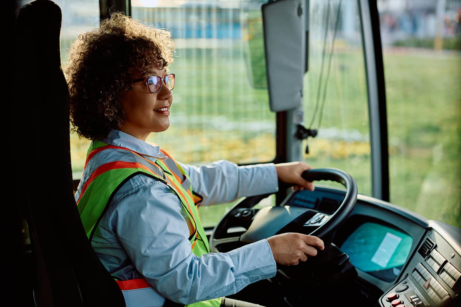 Happy woman driving bus in reverse while looking at rear view mirror.